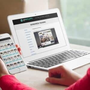 A woman is using a laptop and cell phone to look at a real estate website.