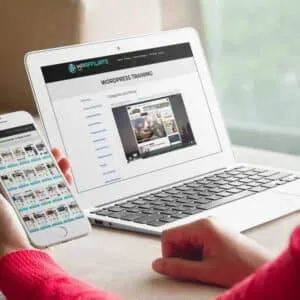 A woman is using a laptop and cell phone to look at a real estate website.